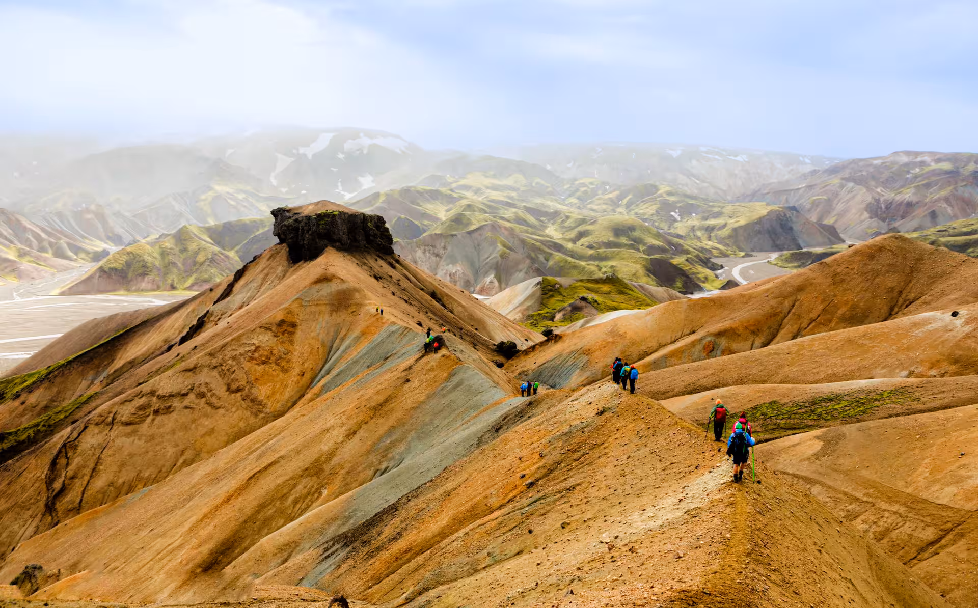 Hikers trekking colorful rhyolite mountains of Landmannalaugar with green moss-covered hills in Iceland
