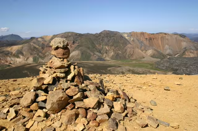 Stone cairn on volcanic summit with colorful Landmannalaugar mountains in background, Iceland