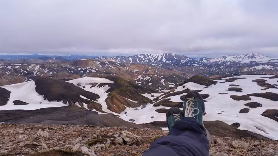 Hiker resting at summit overlooking snow-patched rhyolite mountains of Landmannalaugar, Iceland