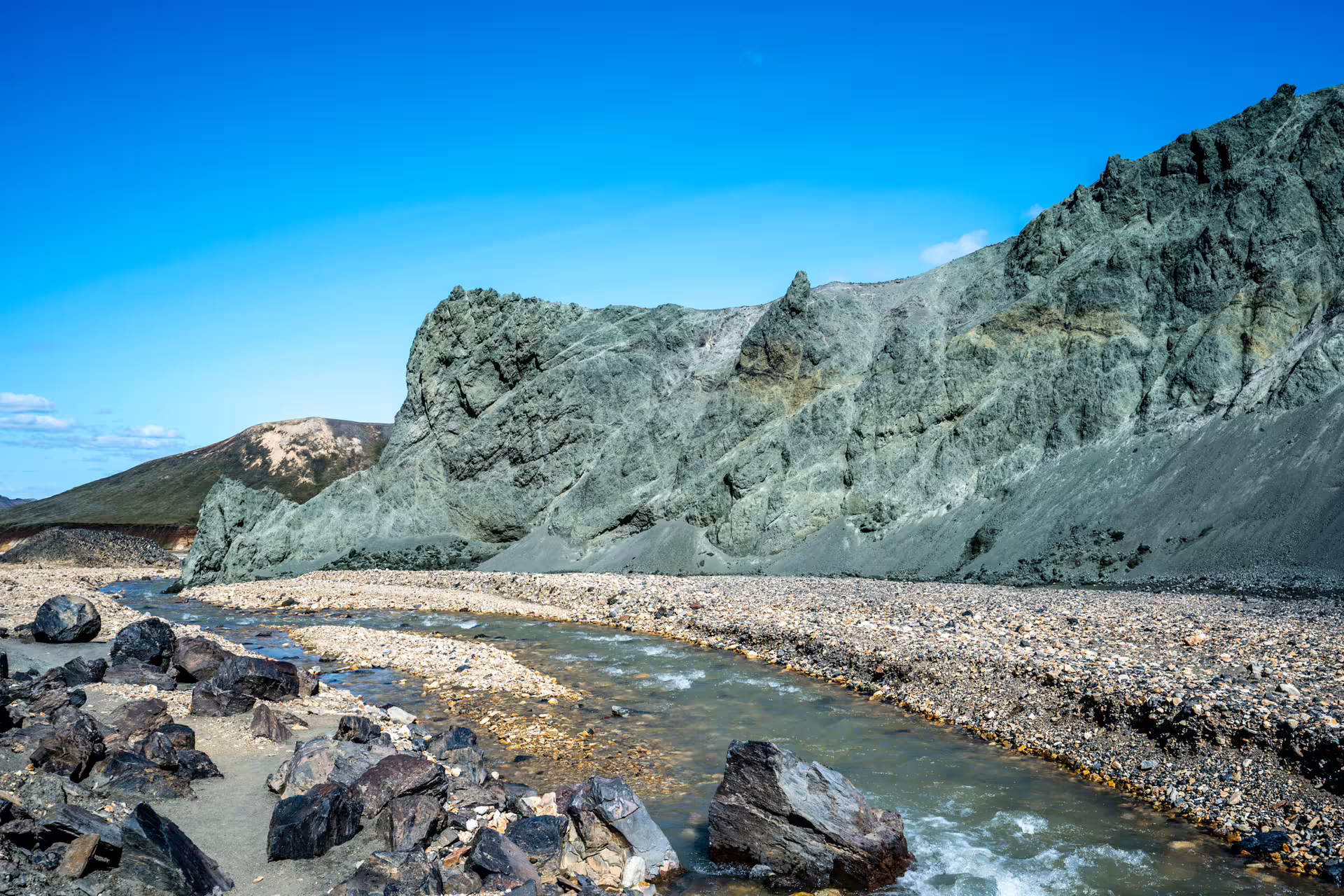 Rocky glacial river flowing through Landmannalaugar's colorful rhyolite mountains under blue sky