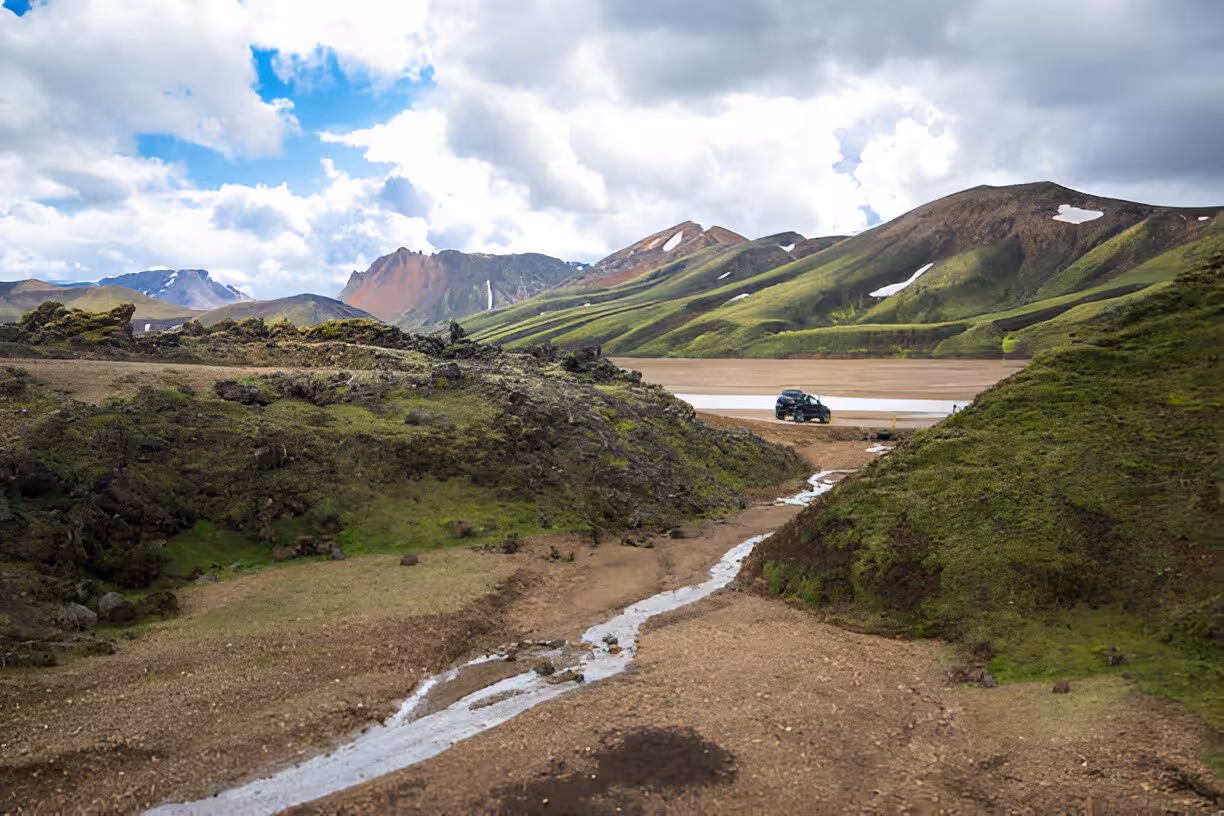 Super jeep crossing a river in Landmannalaugar highland valley with colorful rhyolite mountains