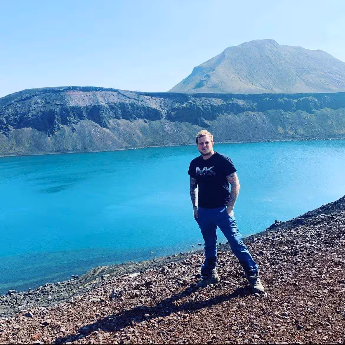 Man standing on volcanic rim overlooking turquoise crater lake at Landmannalaugar, Iceland