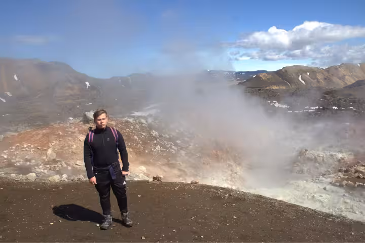 Hiker standing near geothermal steam vents at Landmannalaugar volcanic landscape Iceland