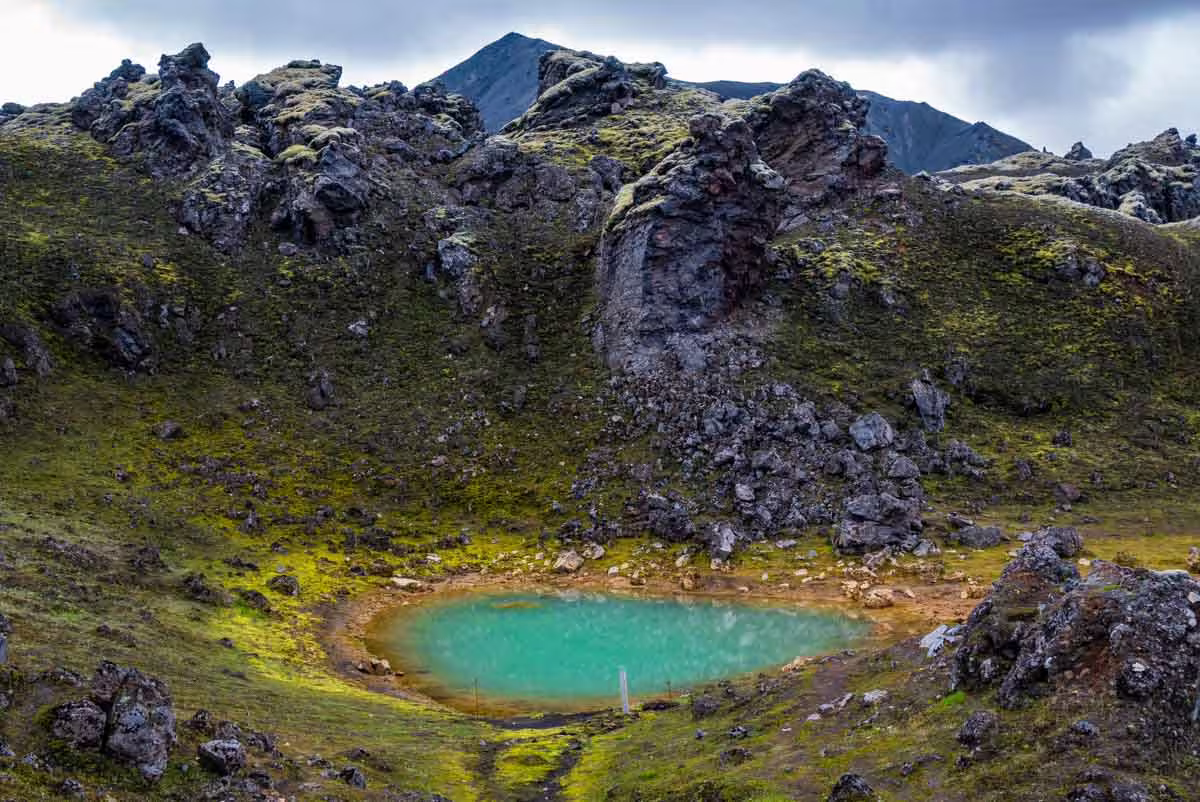 Turquoise crater lake surrounded by mossy lava rocks and volcanic peaks in Landmannalaugar, Iceland
