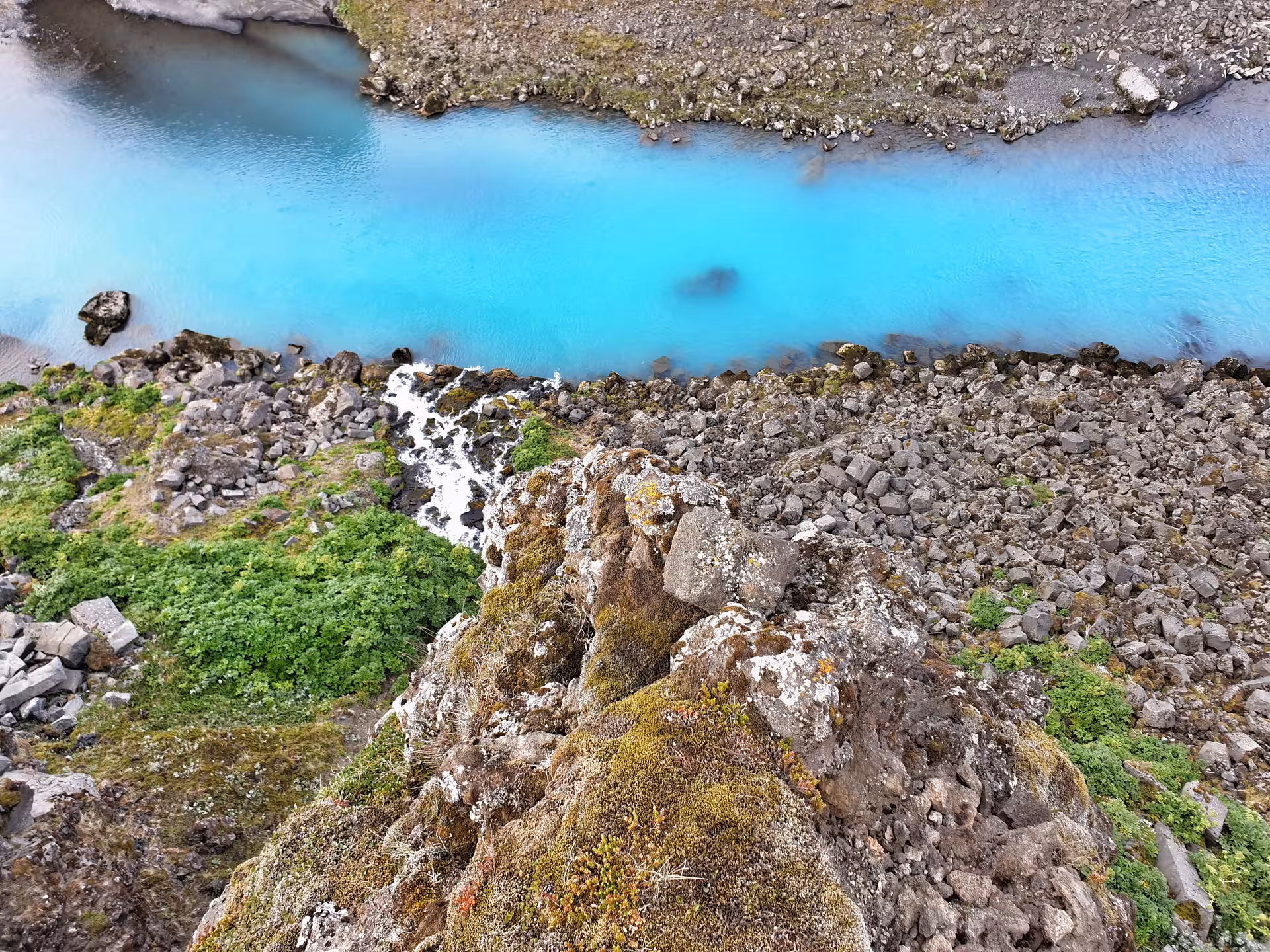 Vivid turquoise glacial river winding through volcanic rocks and green moss in Landmannalaugar, Iceland