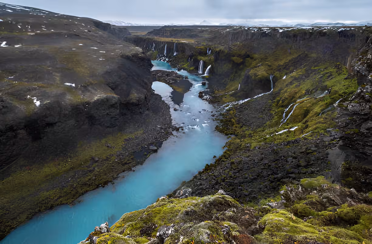 Turquoise glacial river winding through volcanic canyon with cascading waterfalls in Icelandic highlands