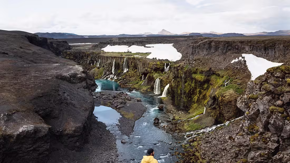 A valley with a river running through it and many small waterfalls pouring into it