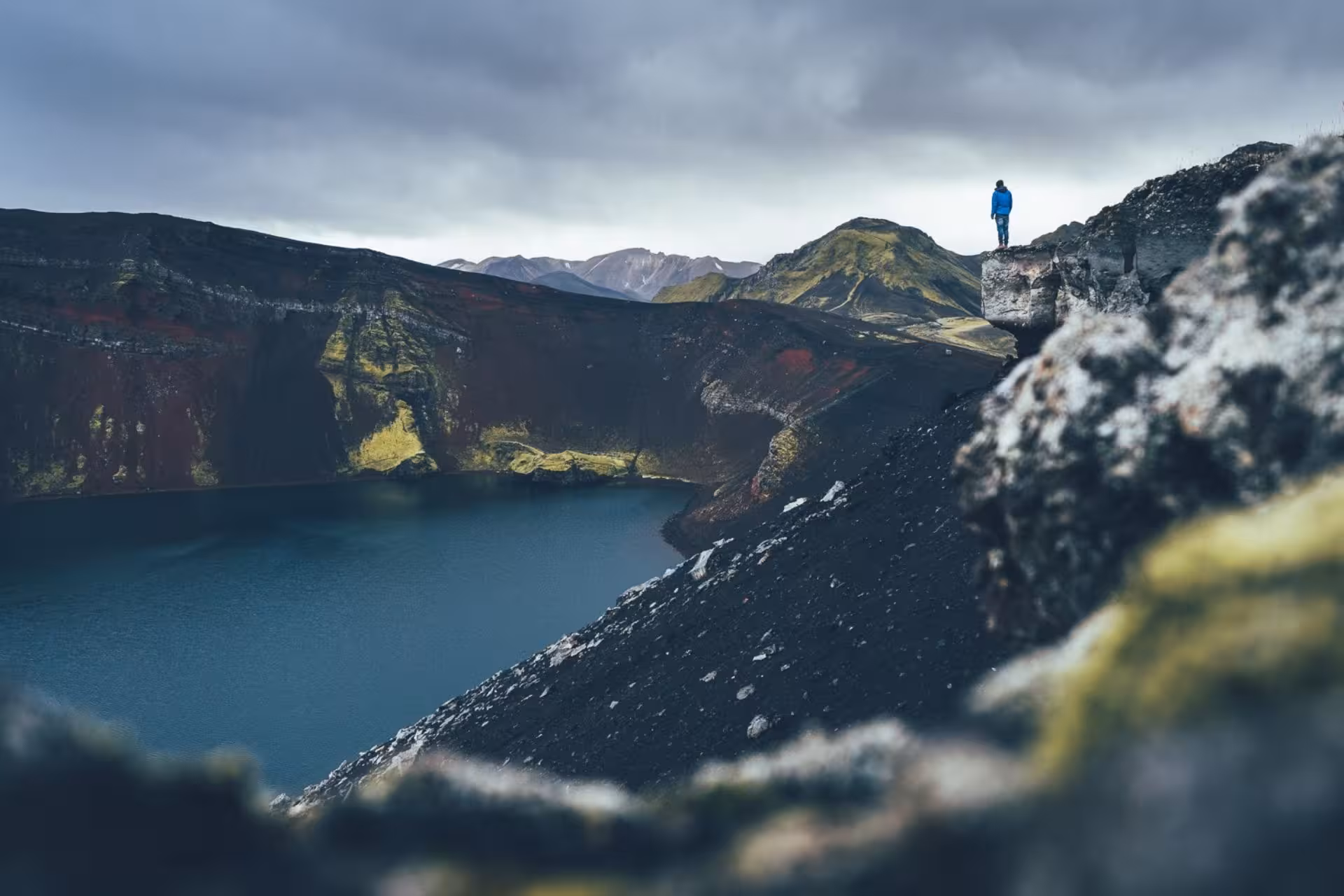 Hiker standing on volcanic crater rim overlooking turquoise lake at Landmannalaugar highlands Iceland