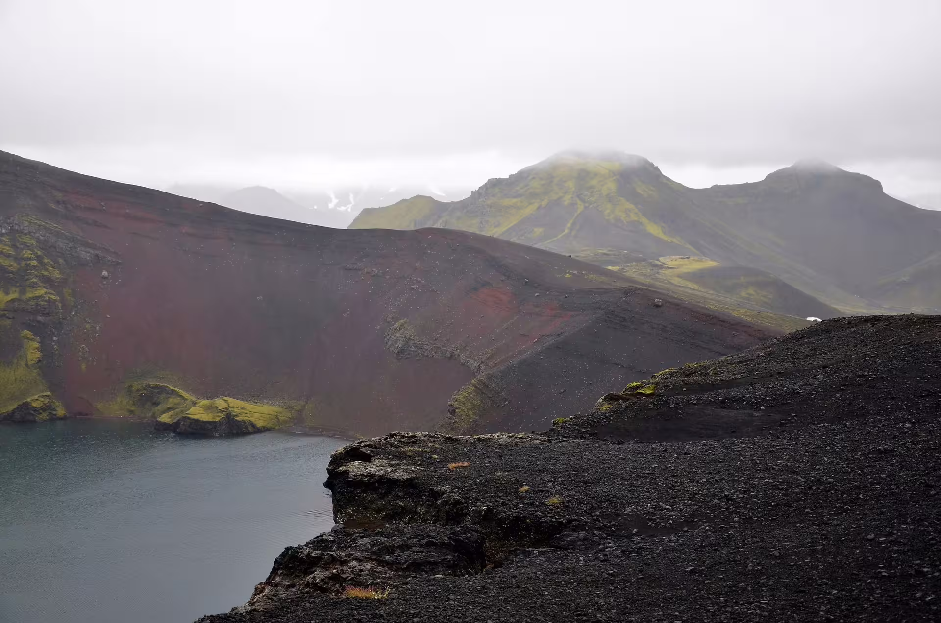 Dramatic volcanic crater lake with red and black lava slopes on Landmannalaugar full-day super jeep tour from Reykjavik Iceland
