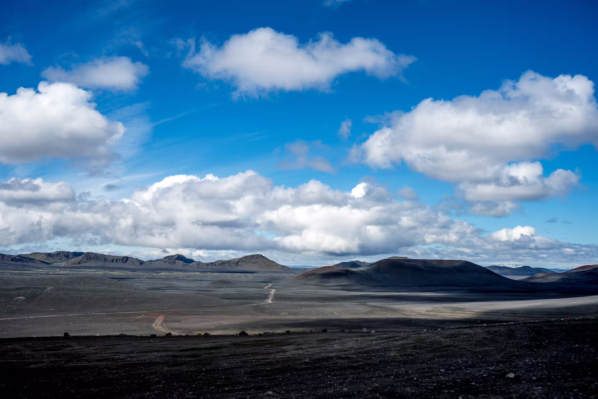 Vast black volcanic highland landscape with cinder cone mountains under blue sky in Landmannalaugar, Iceland