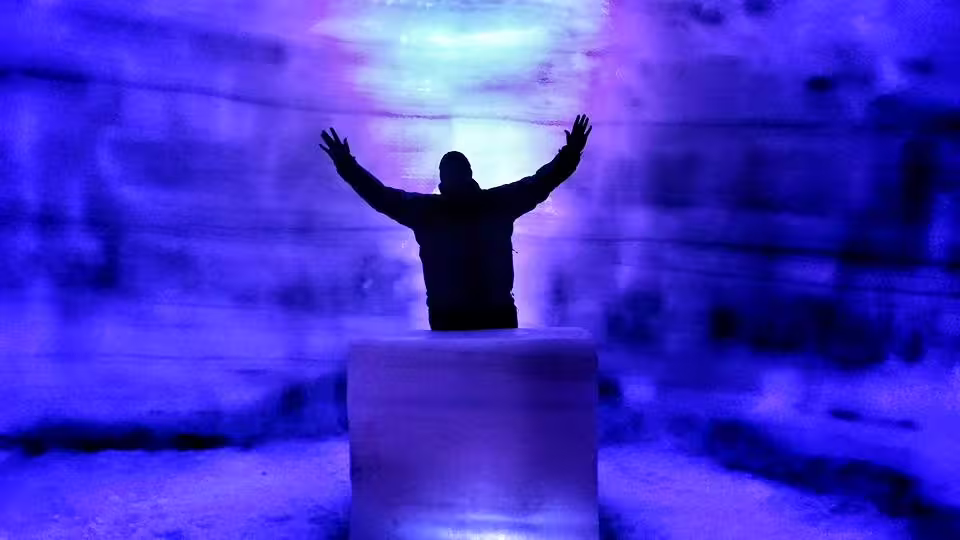 Silhouetted person with arms raised inside blue-lit ice cave at Langjokull Glacier Iceland
