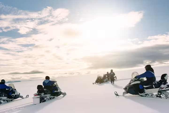 Group of snowmobilers riding across Langjokull glacier snowfield under a bright sun in Iceland