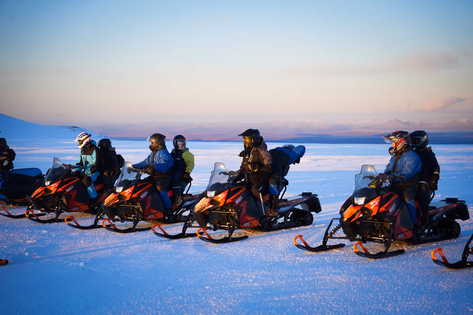 Group of riders on red snowmobiles on Langjokull glacier at sunset, wearing helmets and winter gear