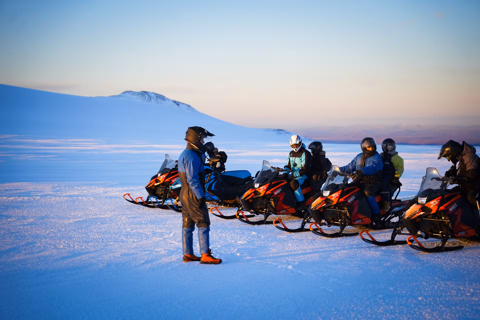 Group of snowmobilers on red Riot snowmobiles lined up on Langjokull glacier at sunset, Iceland