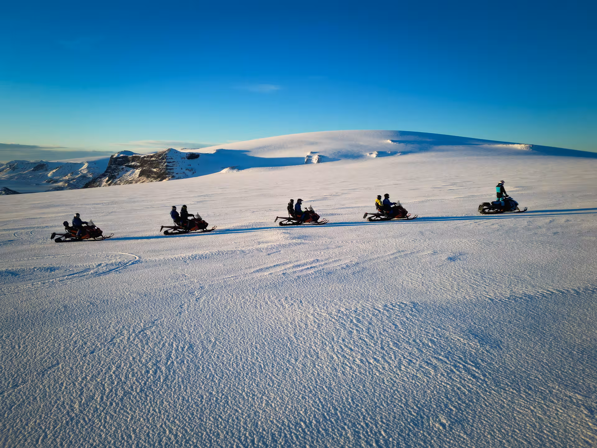Group of snowmobilers riding in a line across Langjokull glacier under a clear blue sky in Iceland
