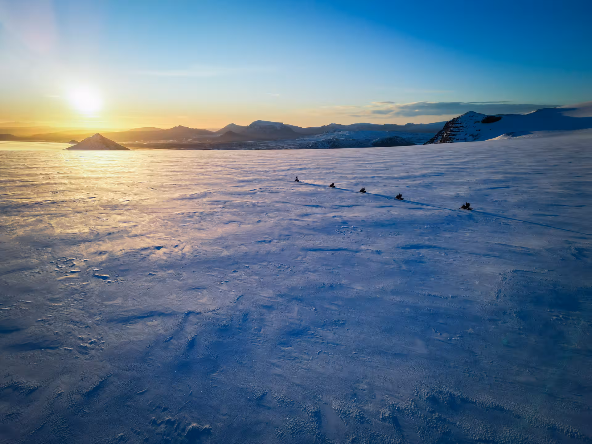 Snowmobilers crossing Langjokull glacier at golden sunset with mountain views from Husafell
