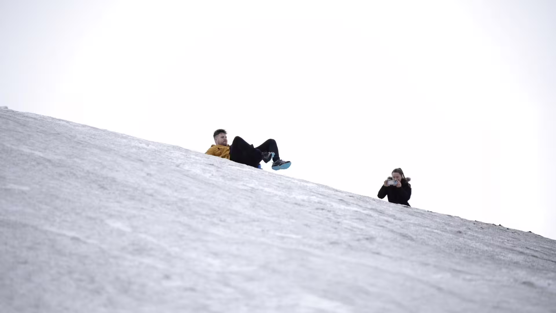Travelers sliding on Langjökull snowfield during Summer Solstice tour from Gullfoss, fun glacier stop in Iceland