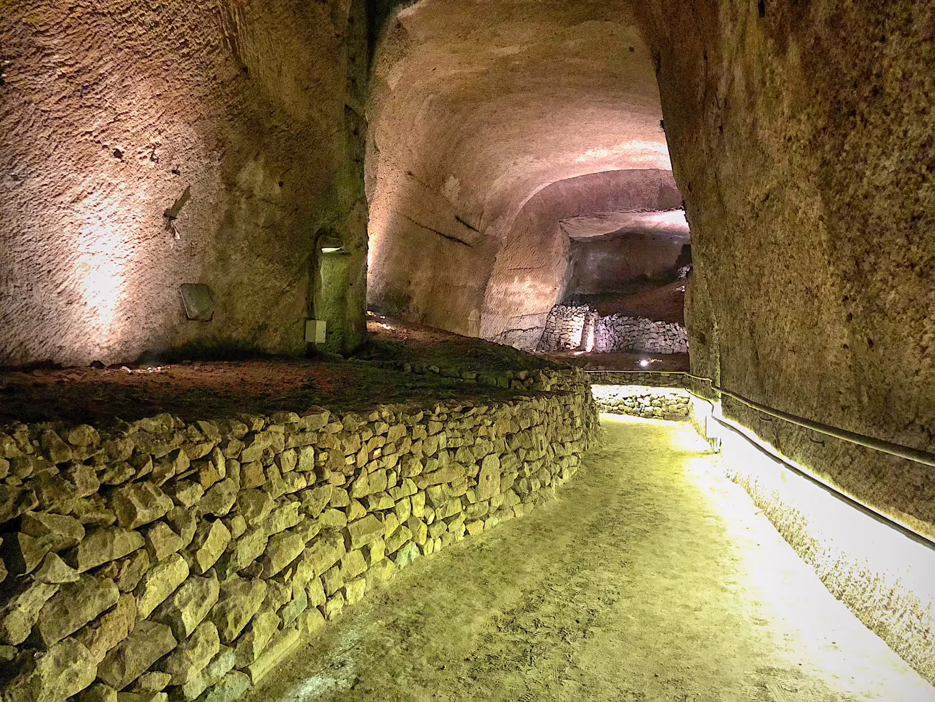 Illuminated stone tunnel of the Decumano Sommerso at Lapis Museum in Naples, showcasing ancient underground passage walls