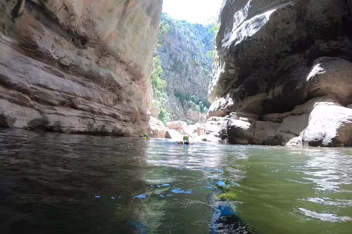 Adventurers swimming through narrow Las Buitreras Canyon gorge with towering limestone walls in Málaga