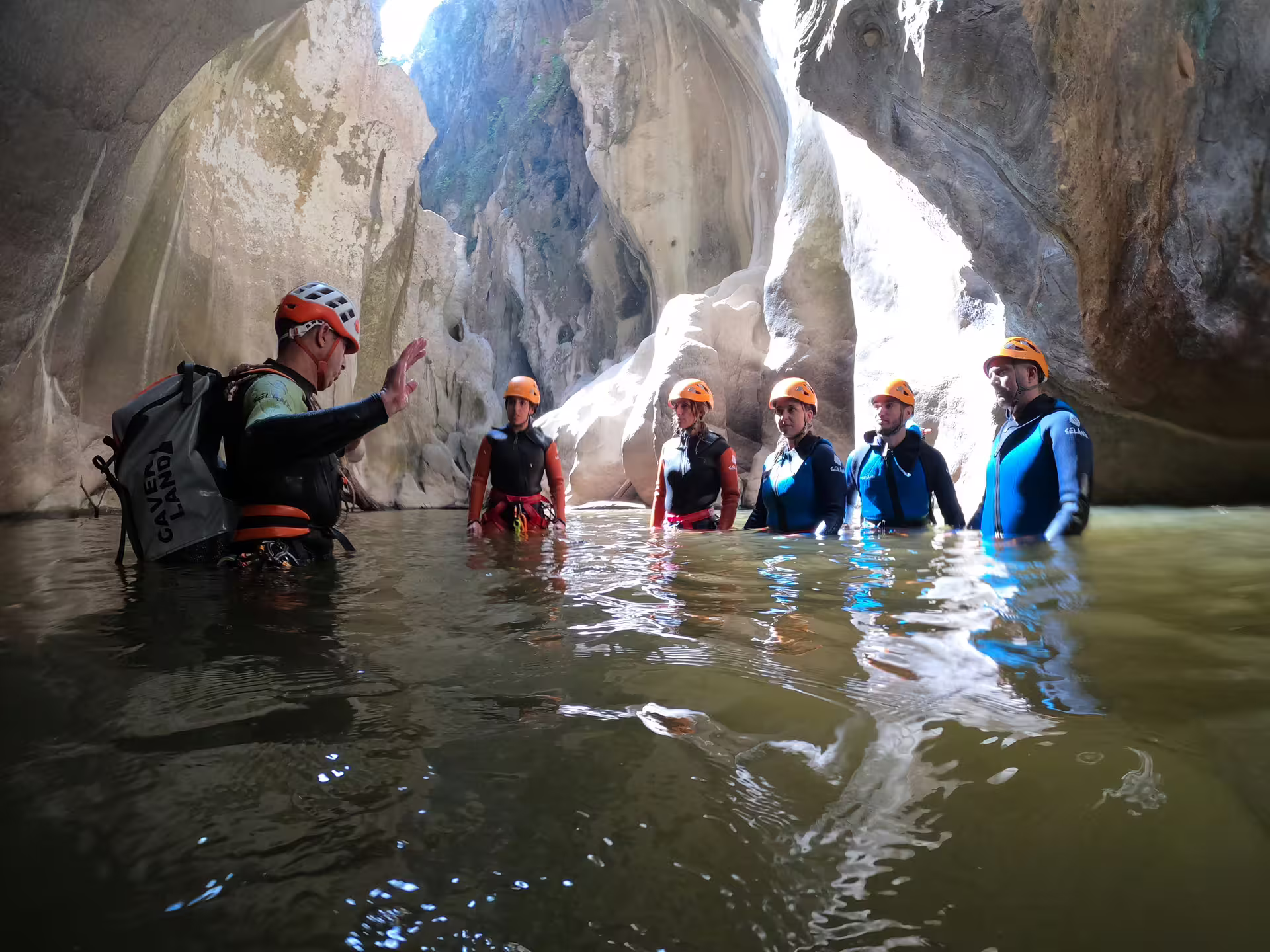 Guide briefing helmeted group wading through Las Buitreras Canyon natural rock archway in Málaga
