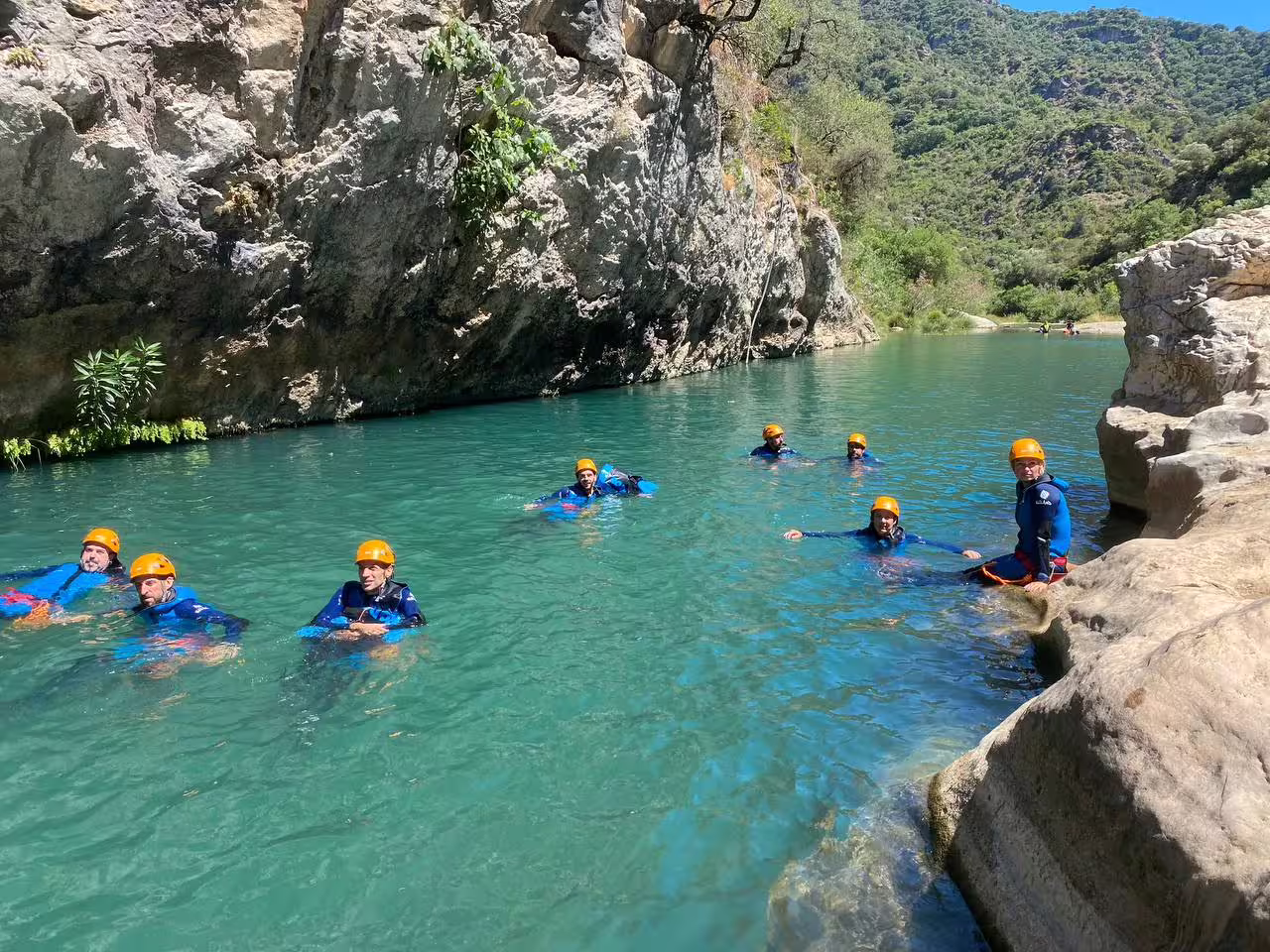 Group of adventure tourists in helmets and wetsuits swimming through turquoise waters of Las Buitreras Canyon Málaga