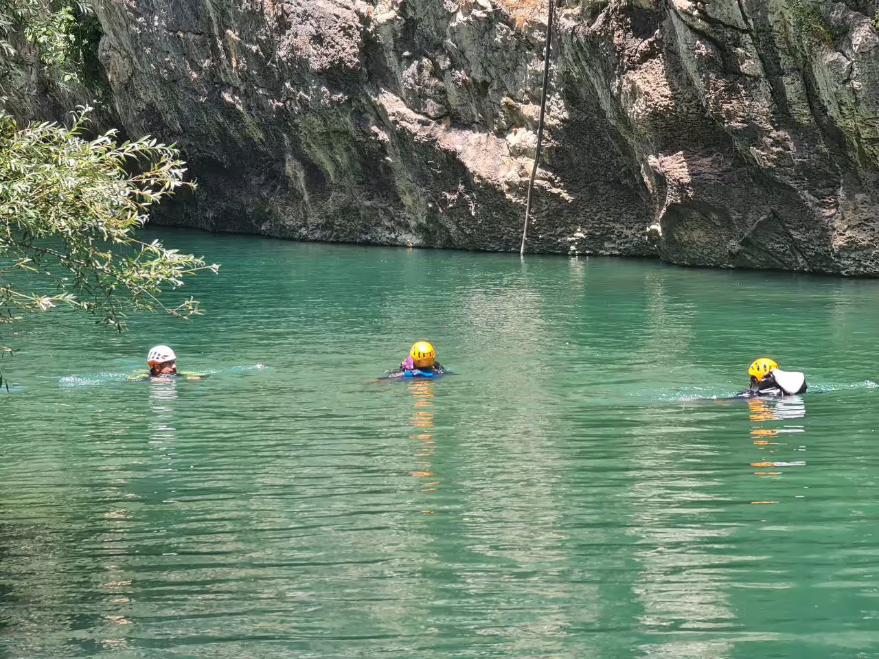 Three helmeted adventurers swimming in turquoise canyon pool during guided Las Buitreras Canyon tour Málaga
