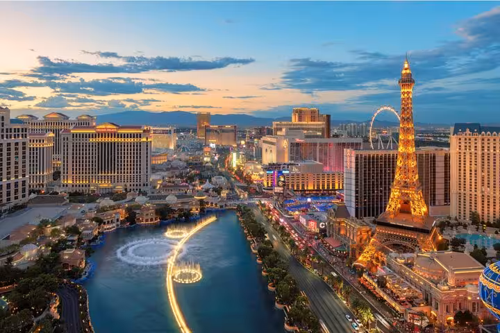 Aerial view of the Las Vegas Strip at dusk with illuminated Eiffel Tower replica and Bellagio fountains