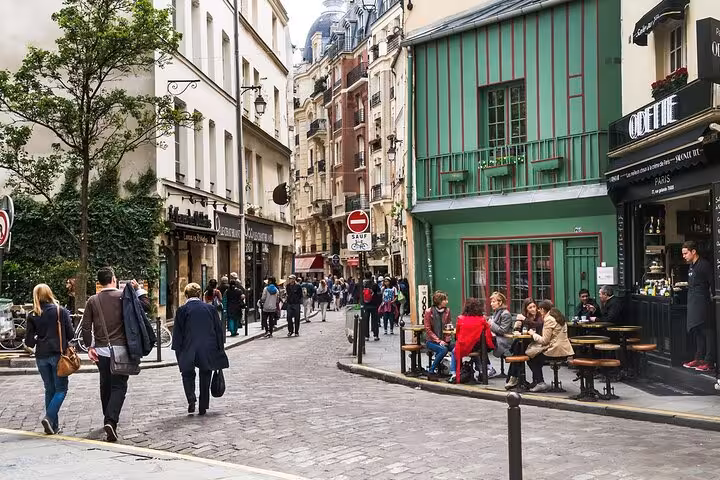 Busy cobblestone street in Paris Latin Quarter with outdoor café seating and green building facade