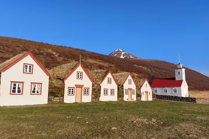 White turf houses with red trim and a small church at Laufas historic farm, North Iceland, with snowy mountain backdrop