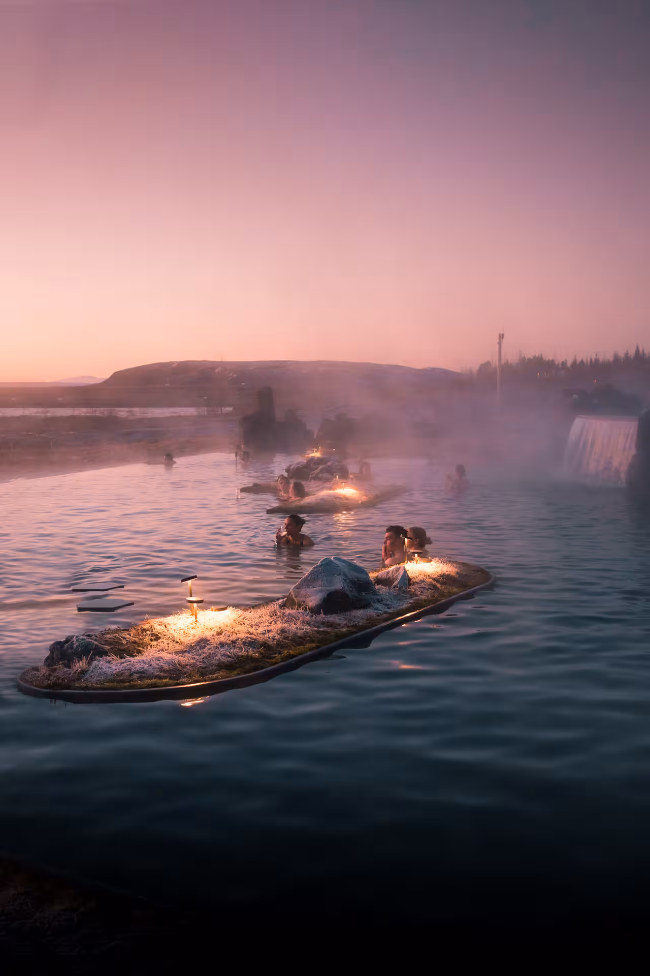Steaming geothermal lagoon at sunset with floating illuminated moss islands and bathers at Laugaras Baths Iceland