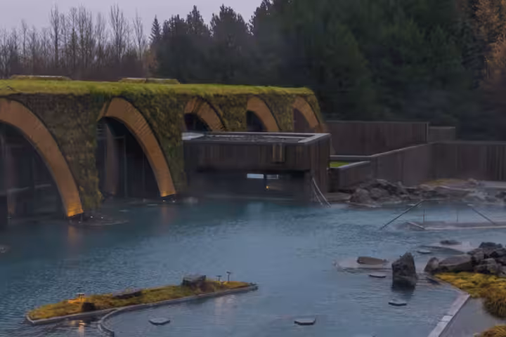 Steaming geothermal pools at Laugaras Baths with moss-covered stone arched bridge in Iceland