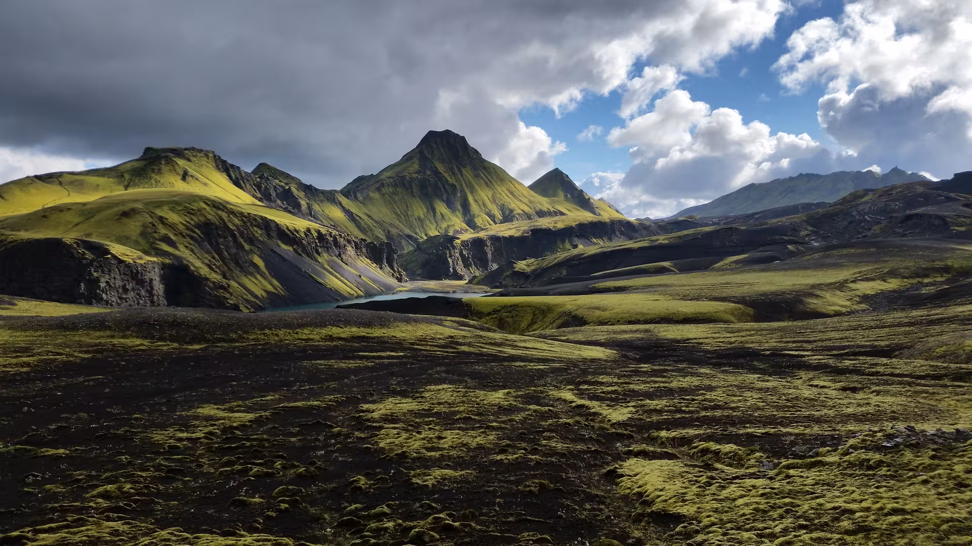 Green moss-covered lava fields with volcanic mountains and glacial lake on Laugavegur trail, Iceland