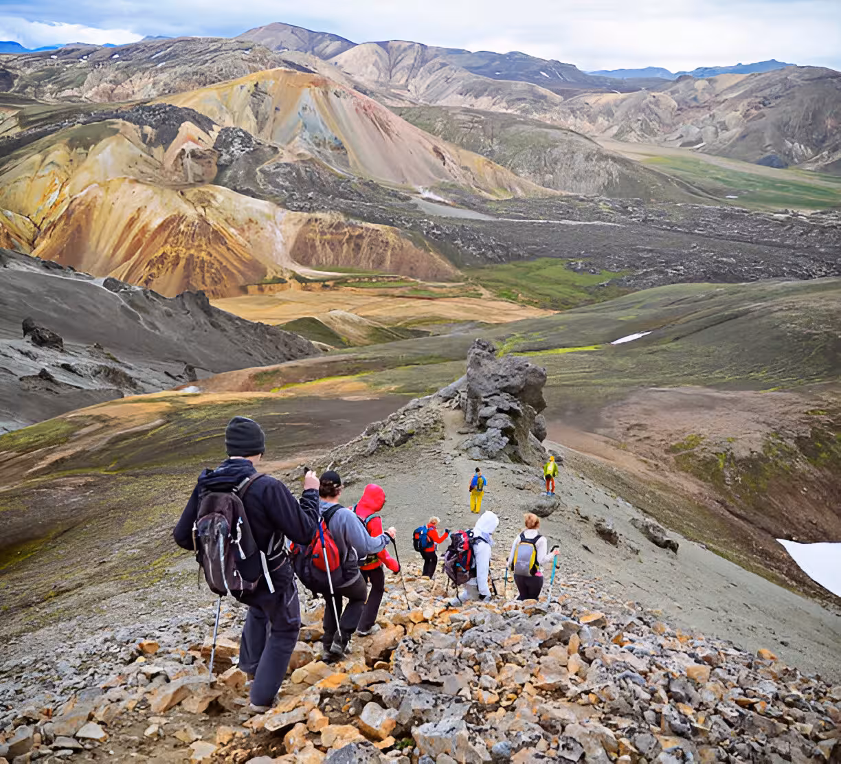 Hikers descending rocky ridge on Laugavegur Trail with colorful rhyolite mountains in Iceland
