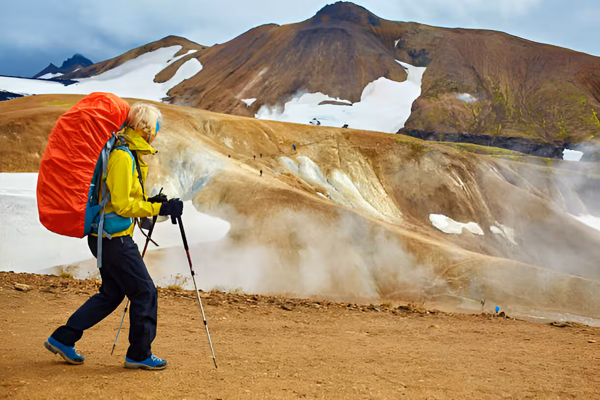 Hiker with large red pack and trekking poles on Laugavegur Trail with colorful Iceland highlands