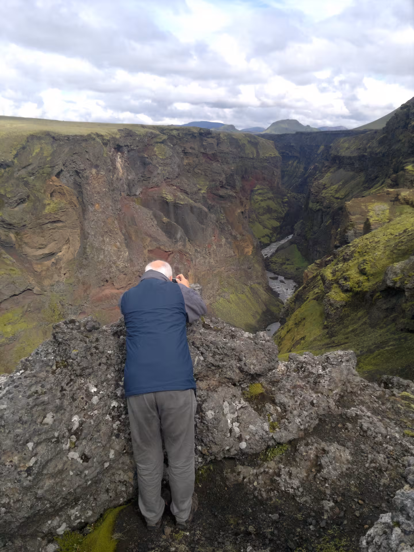 Hiker photographing deep green canyon gorge with river below on Laugavegur trek, Iceland