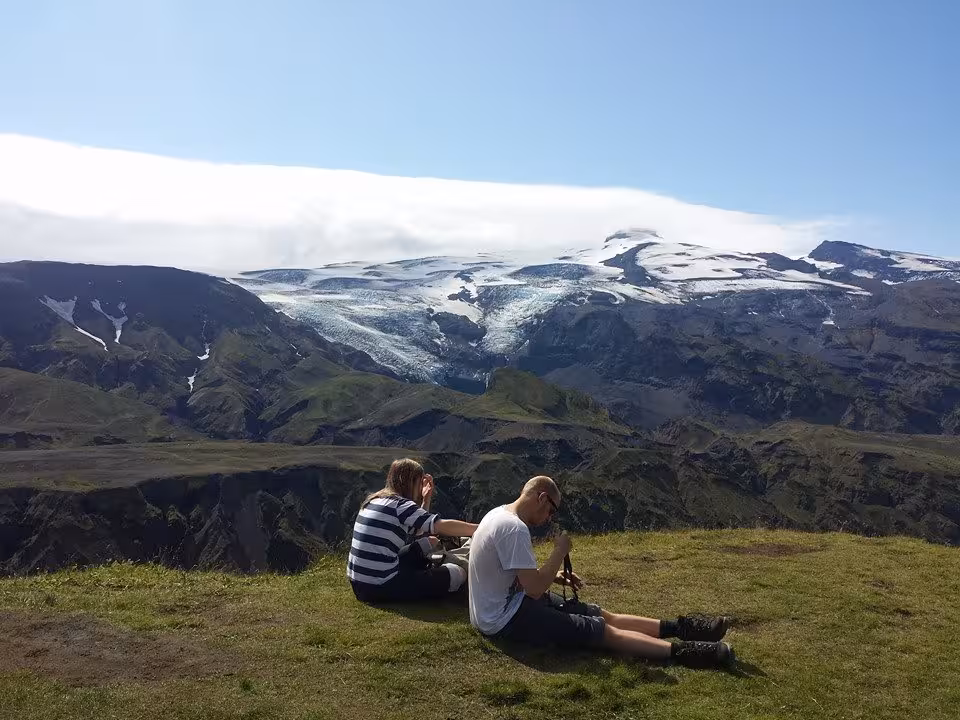 Two hikers resting on grass overlooking Eyjafjallajökull glacier and green valleys on Laugavegur trek