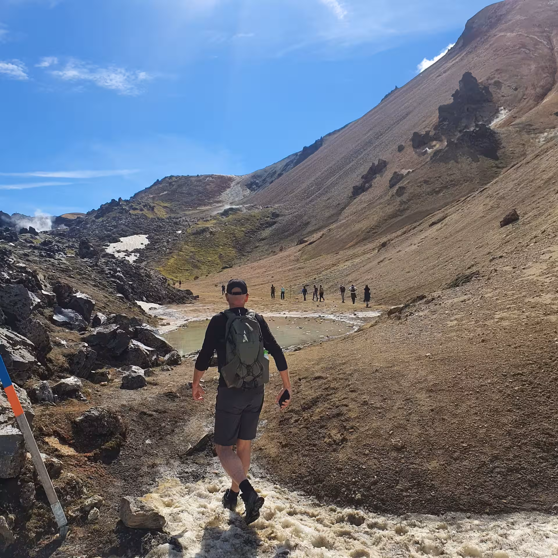 Hiker with backpack walking toward geothermal pool on Iceland's Laugavegur Trek volcanic landscape