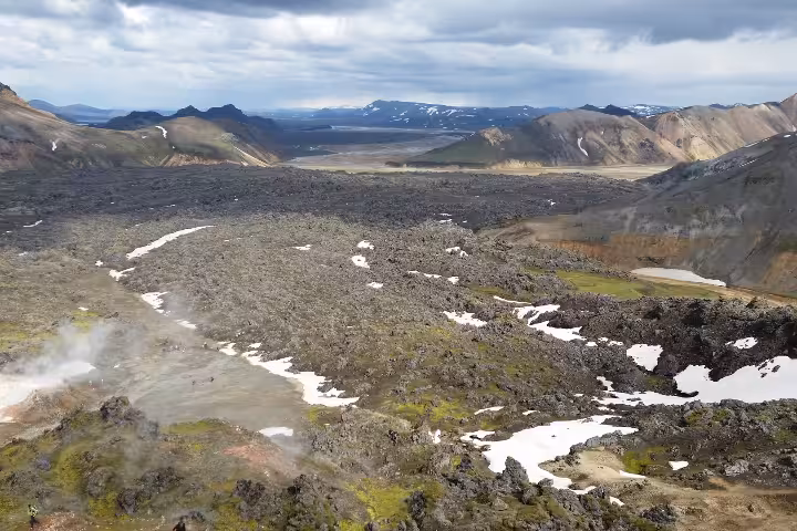 Vast lava field with snow patches and colorful rhyolite mountains in Iceland's highland wilderness