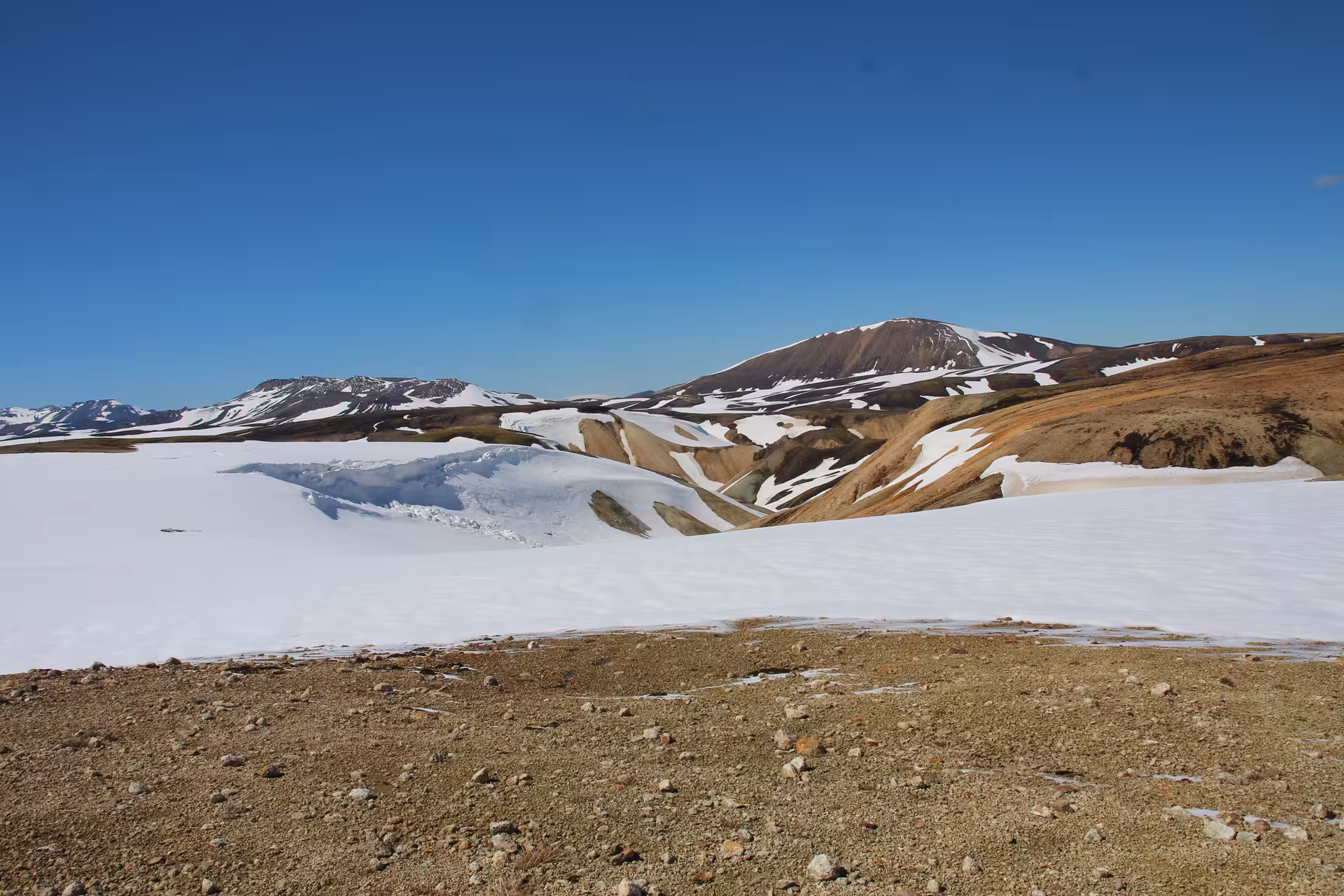 Snow-covered highlands with colorful rhyolite mountains under clear blue sky on Laugavegur trek Iceland