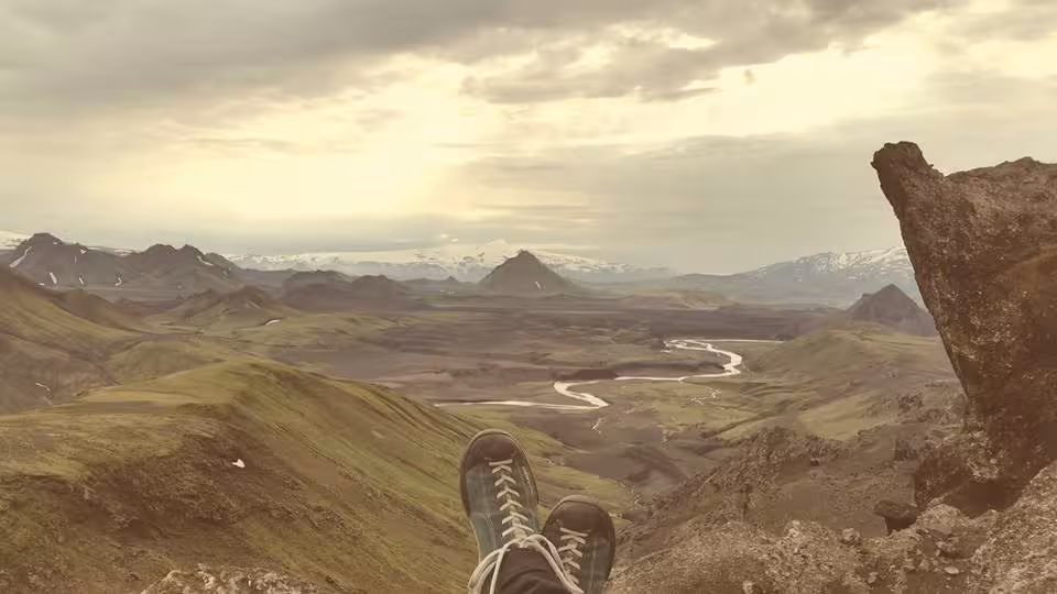 Hiker resting on rocky summit overlooking Laugavegur valley with winding river and snow-capped mountains