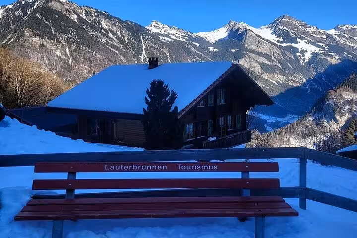Snow-covered Lauterbrunnen chalet with Alps view from a tourist bench on a Swiss Alps tour.