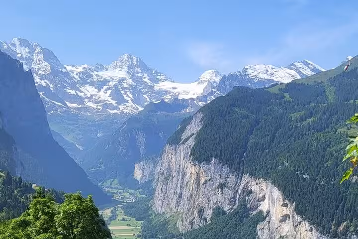 Stunning view of Lauterbrunnen valley with snow-capped Swiss Alps, lush greenery, and blue skies, perfect for a private tour.