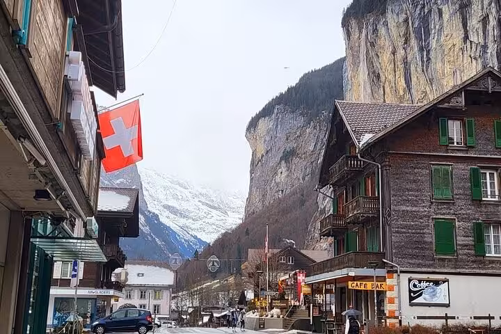 Charming Lauterbrunnen village with Swiss flag, wooden chalets, and towering cliffs in the Swiss Alps tour.