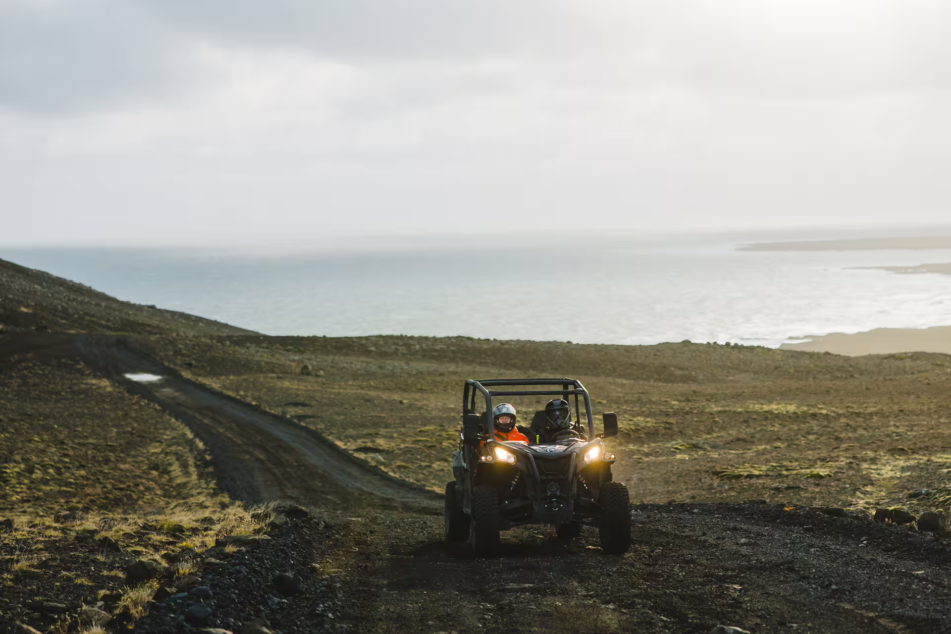 Two riders in helmets driving a buggy on a rugged lava trail with ocean views in Iceland