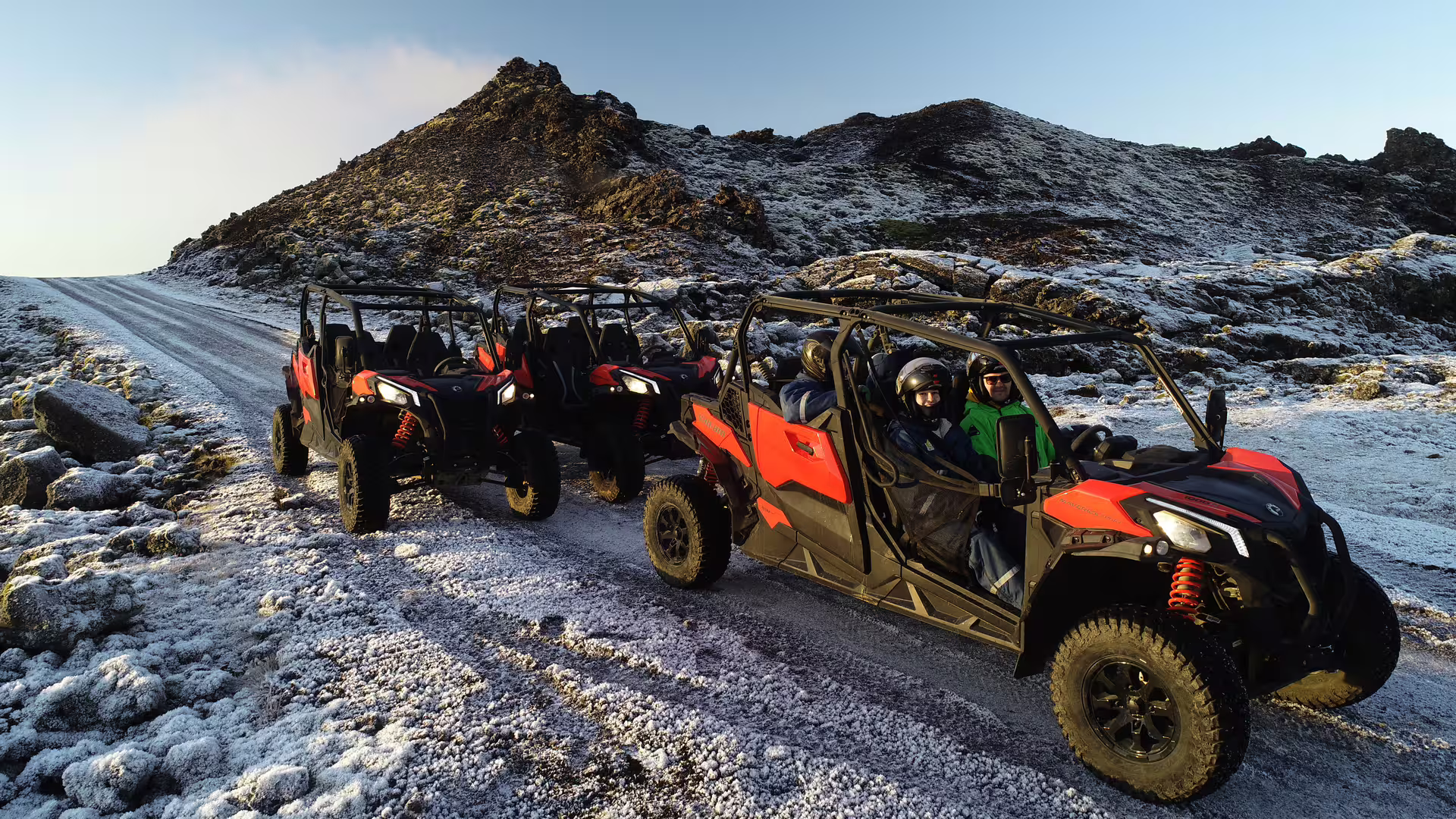 Three red off-road buggies lined up on a snowy lava field trail with rocky volcanic hills in background