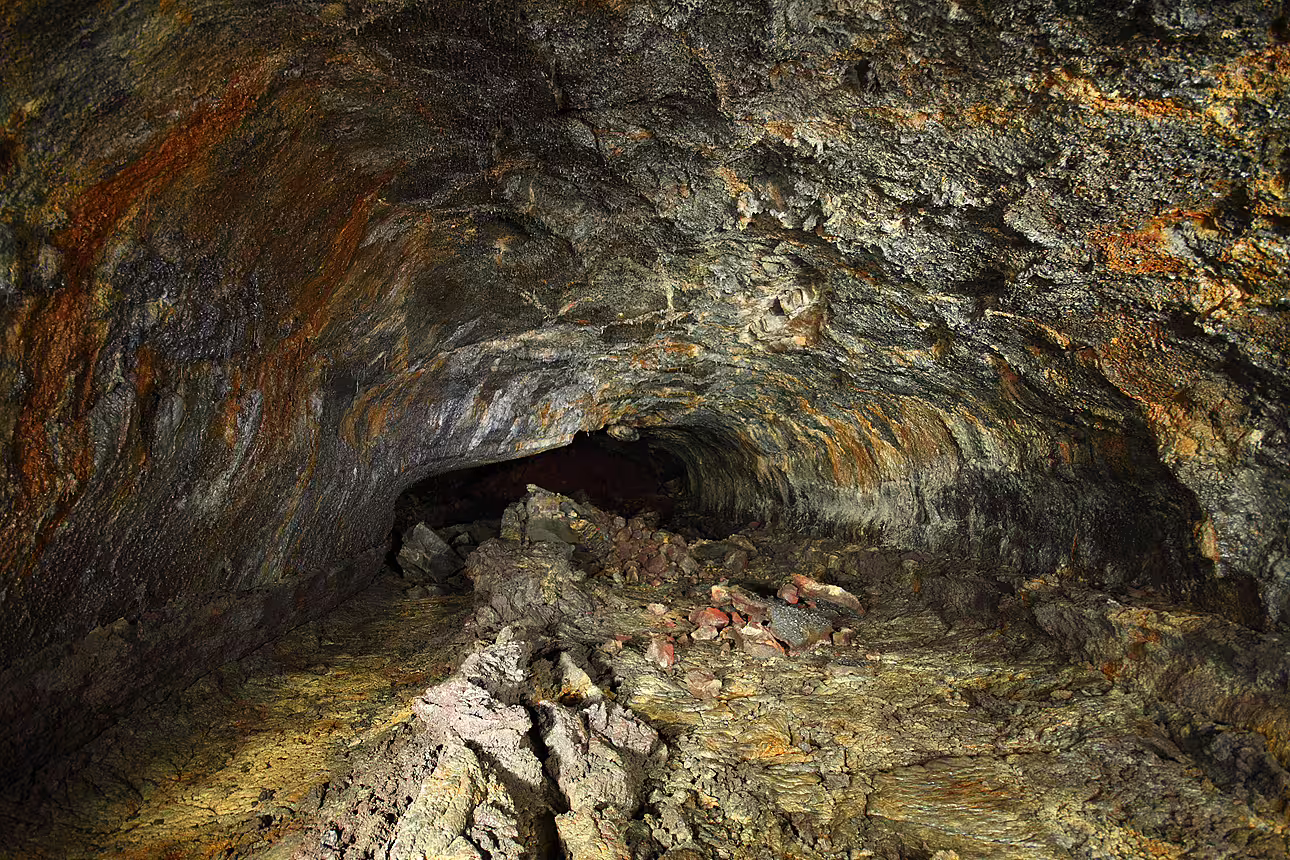 Interior of a volcanic lava cave tunnel with layered rock walls and scattered lava rocks on the floor