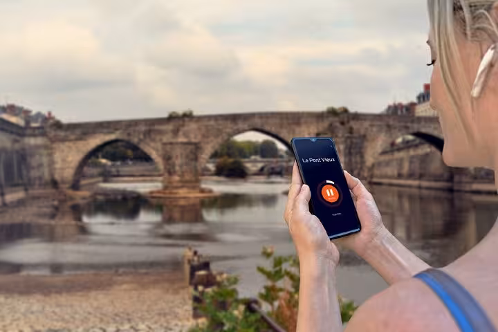 Tourist using audio guide app on smartphone with Le Pont Vieux historic stone bridge in Laval, France