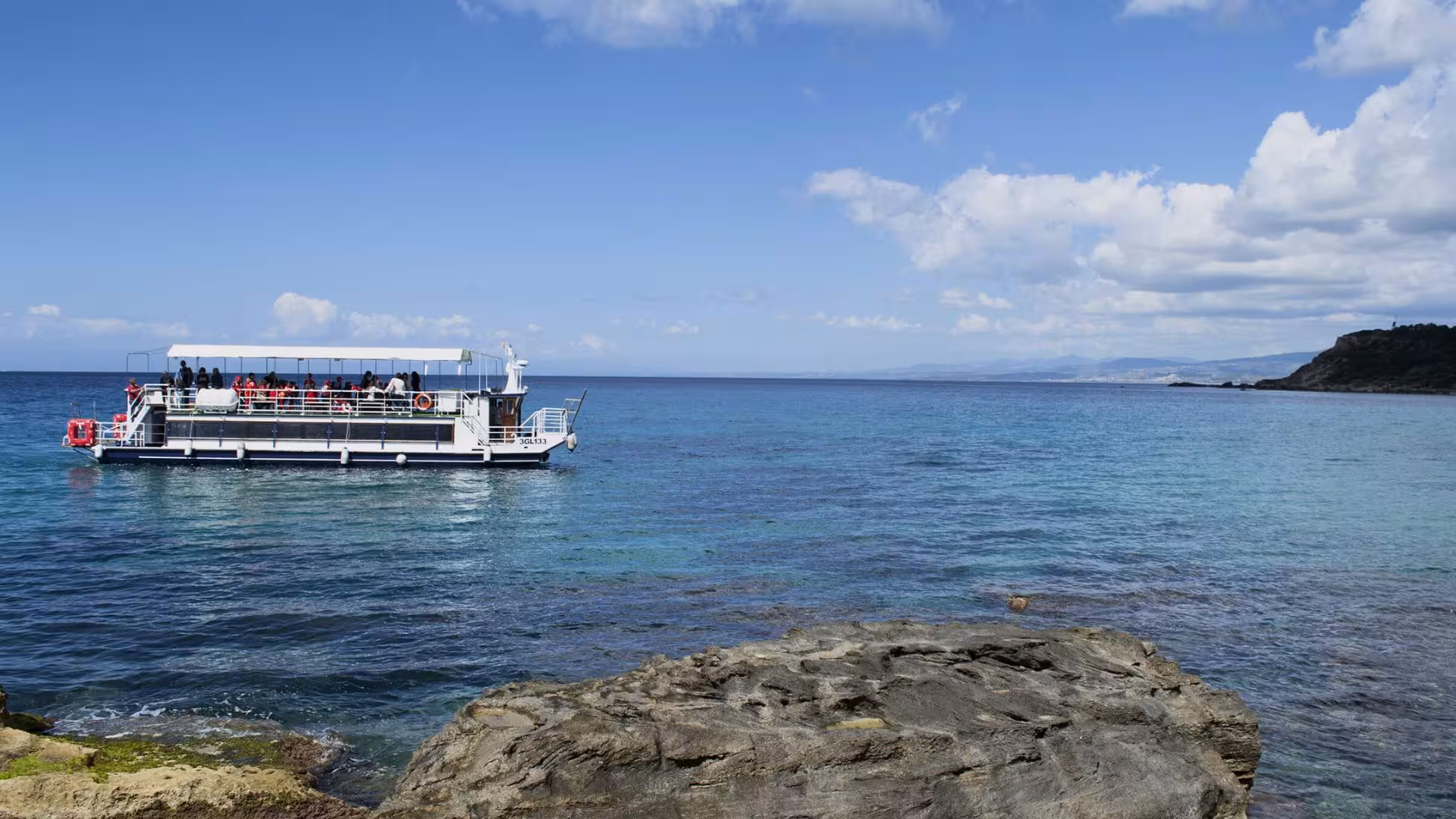 Tour boat with seabed viewing sails in the clear waters of Capo Rizzuto marine area under a sunny blue sky.