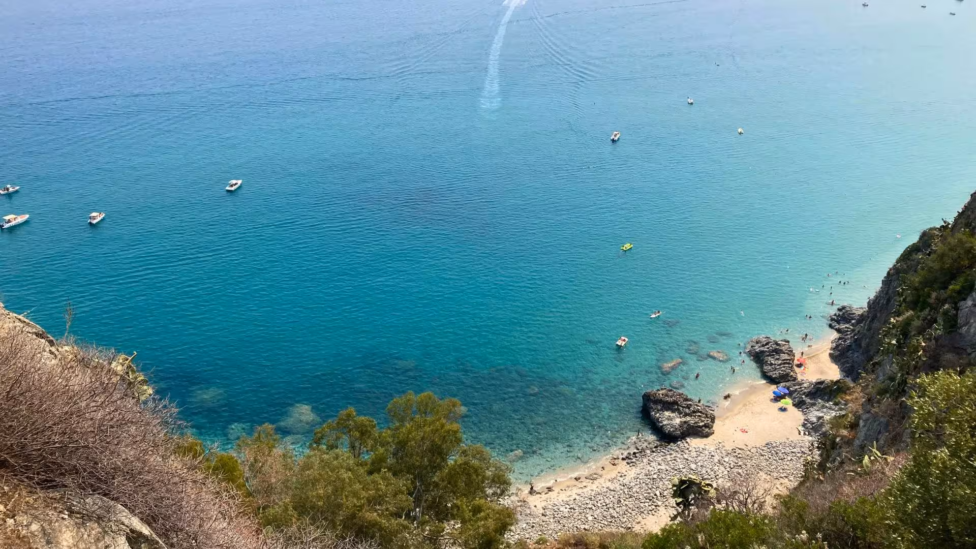 Aerial view of Capo Rizzuto's crystal-clear waters with boats and rocky coastline, ideal for a seabed viewing tour.