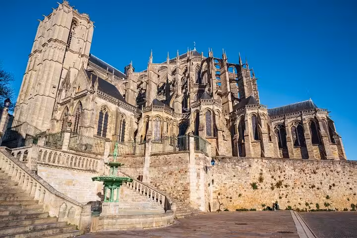 Gothic exterior of Le Mans Cathedral with flying buttresses and a green fountain in the foreground